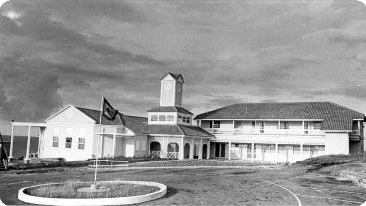 Building with a central clock tower, tiled roof, and a flag flying in front on a roundabout