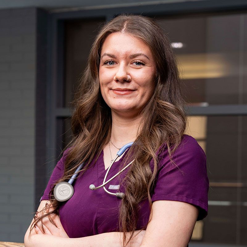Smiling healthcare professional wearing purple scrubs with a stethoscope around her neck