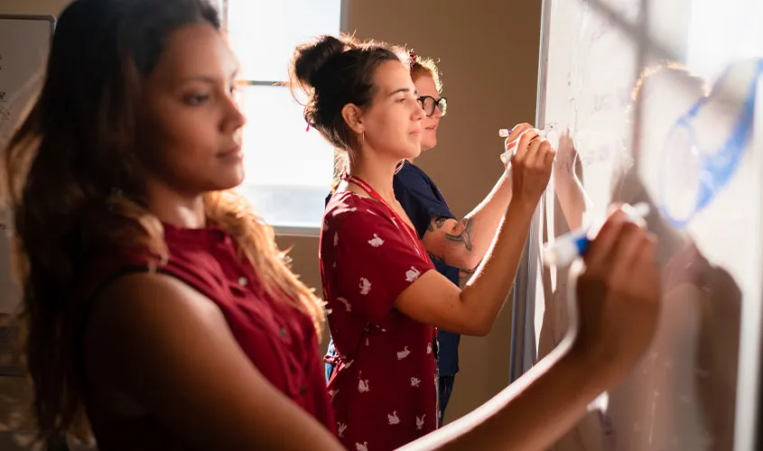 Students at St. George’s University collaborating at a whiteboard in a classroom setting.